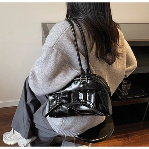 Close-up of black glossy bow shoulder bag with silver hardware and front pockets