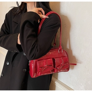 Side view of red patent leather shoulder bag with bow details on black blazer outfit