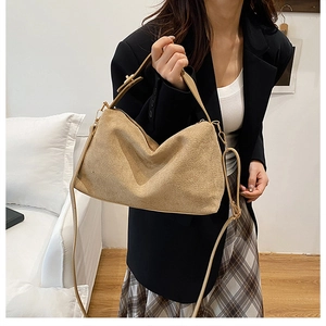 Close-up of khaki suede pillow bag with shoulder strap worn by a model in a blazer