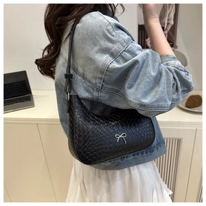 Detail of black woven shoulder bag with silver bow accent on a model for lifestyle view