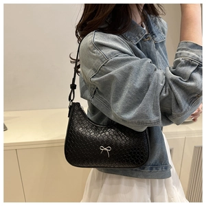 Gros plan d'un sac hobo noir à texture tissée et détail de nœud argenté sur denim