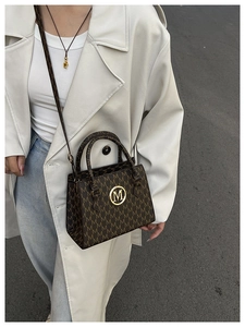 Detail der Umhängetasche mit braunem M-Monogramm und goldener Logo-Schnalle