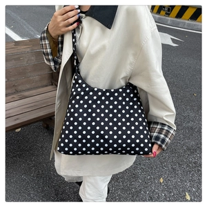 Close-up of a stylish black and white polka dot crossbody bag with a wide fabric strap