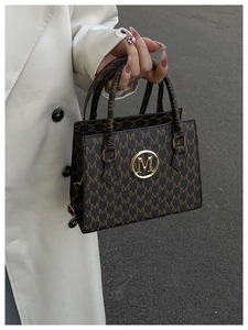 Detail of dark brown tote bag featuring luxury letter pattern and gold M emblem detail