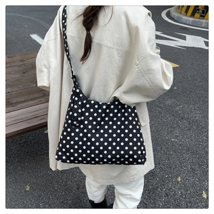 Black and white polka dot crossbody bag with a wide strap shown in a street lifestyle view