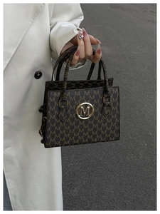 Detailed close-up of dark brown tote bag with M letter pattern and golden logo buckle