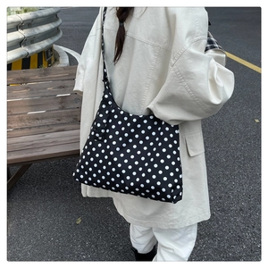 Detailed view of black canvas crossbody bag with white polka dots on model in street setting