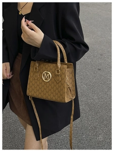 Detail of brown faux leather tote with M-pattern print and gold logo plaque