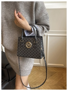Detailansicht der dunkelgrauen Handtasche mit M-Muster und goldenem Logo aus Lederimitat