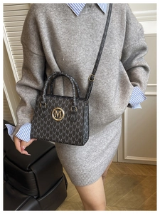 Close-up of black handbag with golden M logo and monogram pattern on model's shoulder