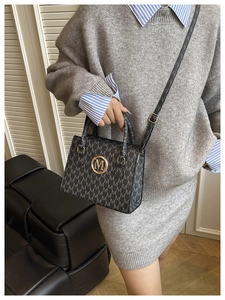 Detail of black tote bag with M-pattern print and golden circular metal M logo