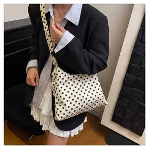 Polka dot crossbody bag styled with a wide strap on a model wearing a black blazer