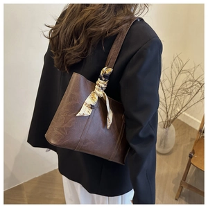 Detail der dunkelbraunen Leder-Shopper-Tasche mit Seidenschal-Dekor am Griff im Studio