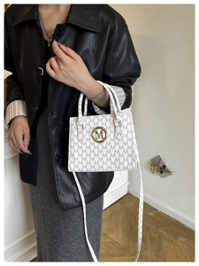 Close-up of white crossbody bag featuring letter M monogram pattern and gold metal logo
