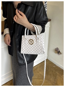 Detail of white PU leather shoulder bag with M-pattern printing and golden logo