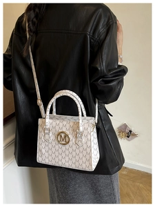 Dettaglio della borsa monogramma bianca con logo M dorato portata a spalla su una giacca nera