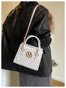 Detail shot of white crossbody bag with grey M pattern print and gold logo hardware