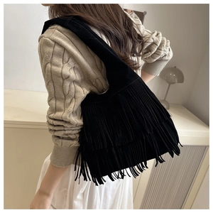 Dettaglio di una borsa hobo nera in pelle scamosciata con lunghe frange su un maglione beige