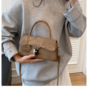 Brown vintage leather shoulder bag featuring a unique lock clasp and round charm tag