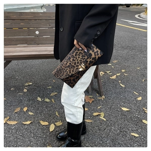Chic leopard print envelope clutch featuring a wavy gold metallic buckle held by a model