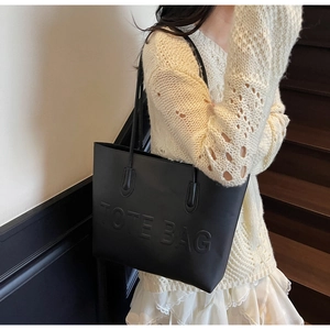 Close-up of black leather tote bag with embossed lettering and long shoulder straps