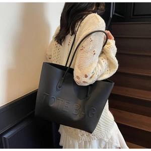 Detail of black matte leather tote bag with embossed TOTE BAG text and long shoulder strap