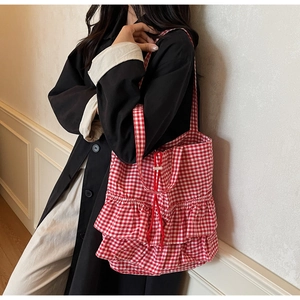 Detailed view of red plaid tote bag with ruffle trim and drawstring closure on shoulder