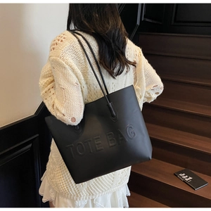 Close-up of black matte leather tote bag featuring 3D embossed letters and long straps