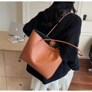 Close-up of the embossed TOTE BAG lettering on a brown leather shoulder bag detail