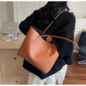 Brown tote bag with embossed lettering detail worn by model in a cozy office setting
