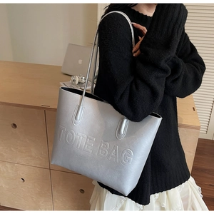 Detail of silver metallic tote bag featuring a prominent embossed letter design
