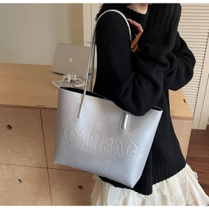 Detail of silver tote bag with embossed lettering carried over the shoulder in a scene