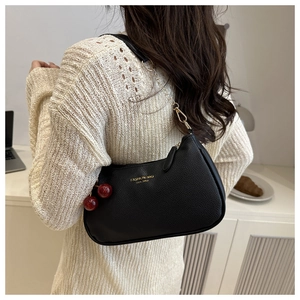 Detail of black litchi grain leather underarm bag with gold chain and cherry charm