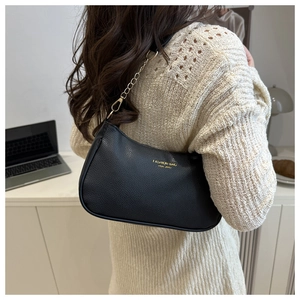 Detail of black lychee texture leather shoulder bag with gold chain strap on knit sweater