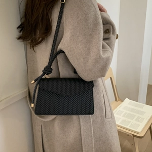 Minimalist black woven shoulder bag featuring a V-shaped pattern and knotted strap