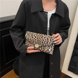 Leopard print envelope clutch with gold heart clasp carried by model in black coat