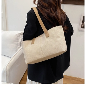Detailed texture of large beige canvas tote bag with brown leather handles worn by model