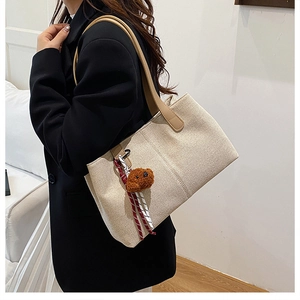 Detail of beige tote bag with leather strap and plush bear charm on a female model