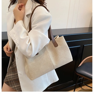 Detail of canvas tote bag with brown leather handles worn in a commuter setting