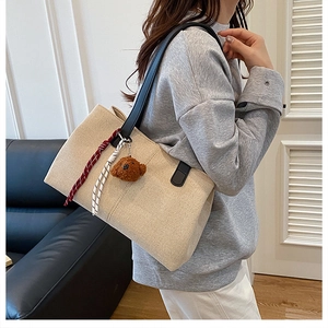 Detailed side view of beige woven tote bag with teddy bear charm and black straps