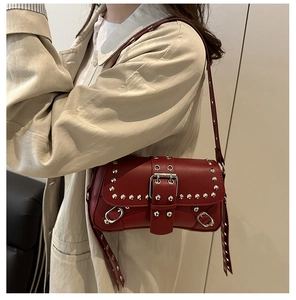 Detalle del bolso punk rojo con tachuelas plateadas y hebilla sobre una gabardina