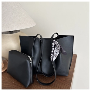 Detail of black tote bag set with matching pouch and patterned silk scarf on a wooden table