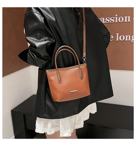 Brown lychee leather bucket bag detail showing the adjustable strap and metallic logo