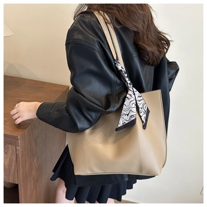 Detail of a beige leather tote bag with a patterned scarf on handle shown on a model