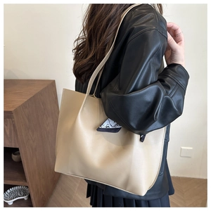 Detail of a beige tote bag with decorative silk scarf worn on a model shoulder