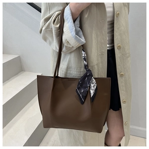 Detail of dark brown leather tote bag with elegant leaf pattern silk scarf on handle
