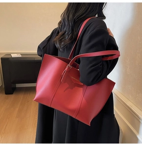 Détail du sac cabas en cuir rouge avec lettrage doré porté sur un manteau noir