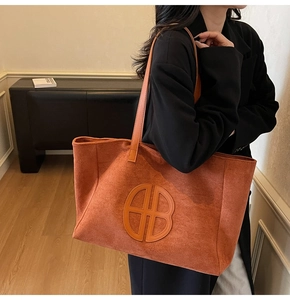 Close-up of large orange-brown suede tote bag with circular logo detail worn by a model