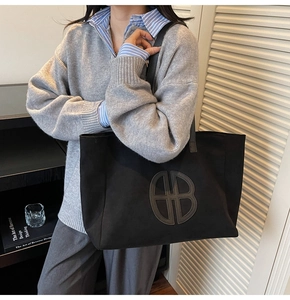 Detail of black large capacity tote bag with geometric logo on a shoulder model