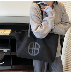 Detail of black canvas tote bag featuring a circular AB monogram logo on a minimalist background